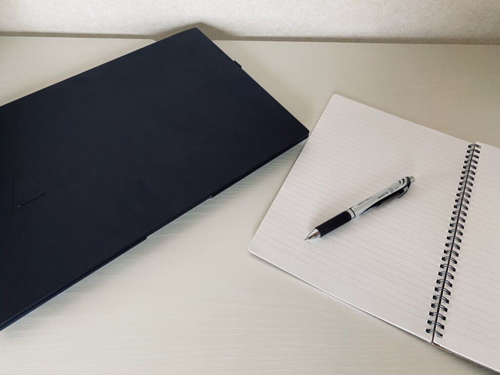 薄型ノートPCとリングノート、ペンを机に置いた在宅ワークの作業風景