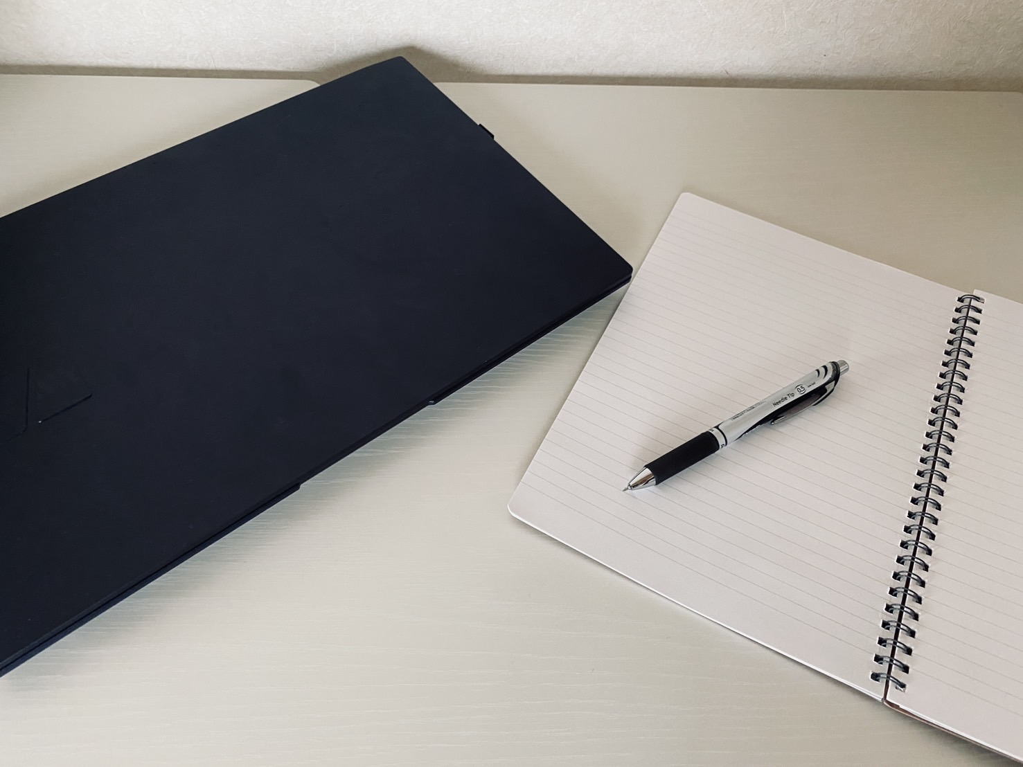 薄型ノートPCとリングノート、ペンを机に置いた在宅ワークの作業風景