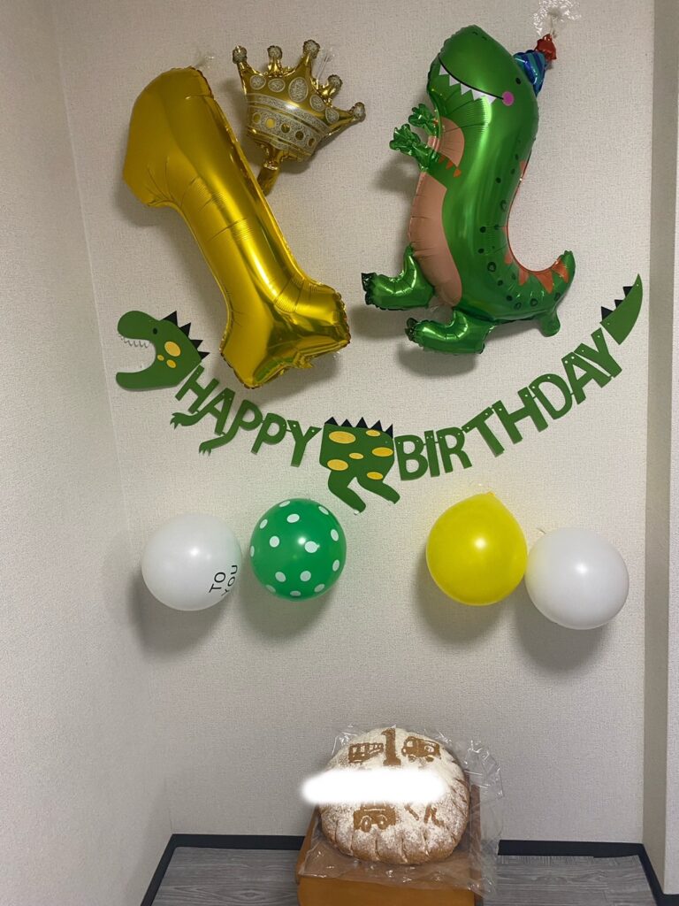恐竜と王冠のバルーンで飾った壁面に、1の風船と一升パンを並べた1歳誕生日の飾り付けの様子