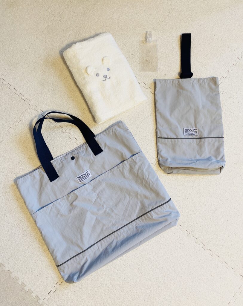 誰でも通園制度の体験記の表紙用に、保育園バッグとシューズケース、氏名札とおしりふき用タオルを並べたフラットレイの写真。