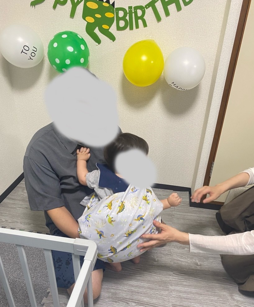 恐竜柄の布で包んだ一升パンを背負う1歳児を家族が支える瞬間の記録