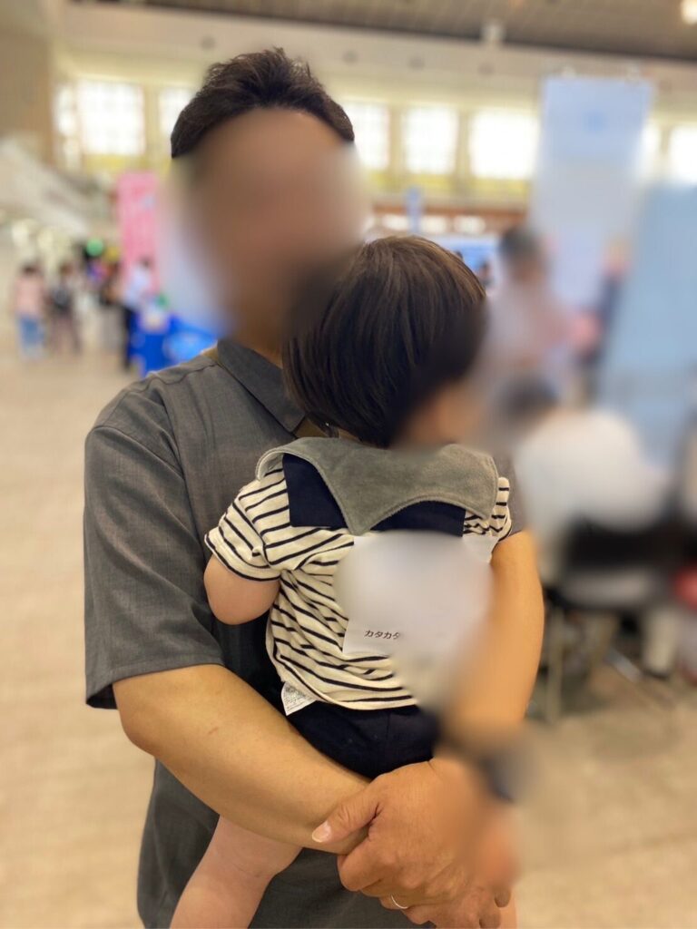 会場ロビーでゼッケンを貼った子どもを父が抱っこしているところ
