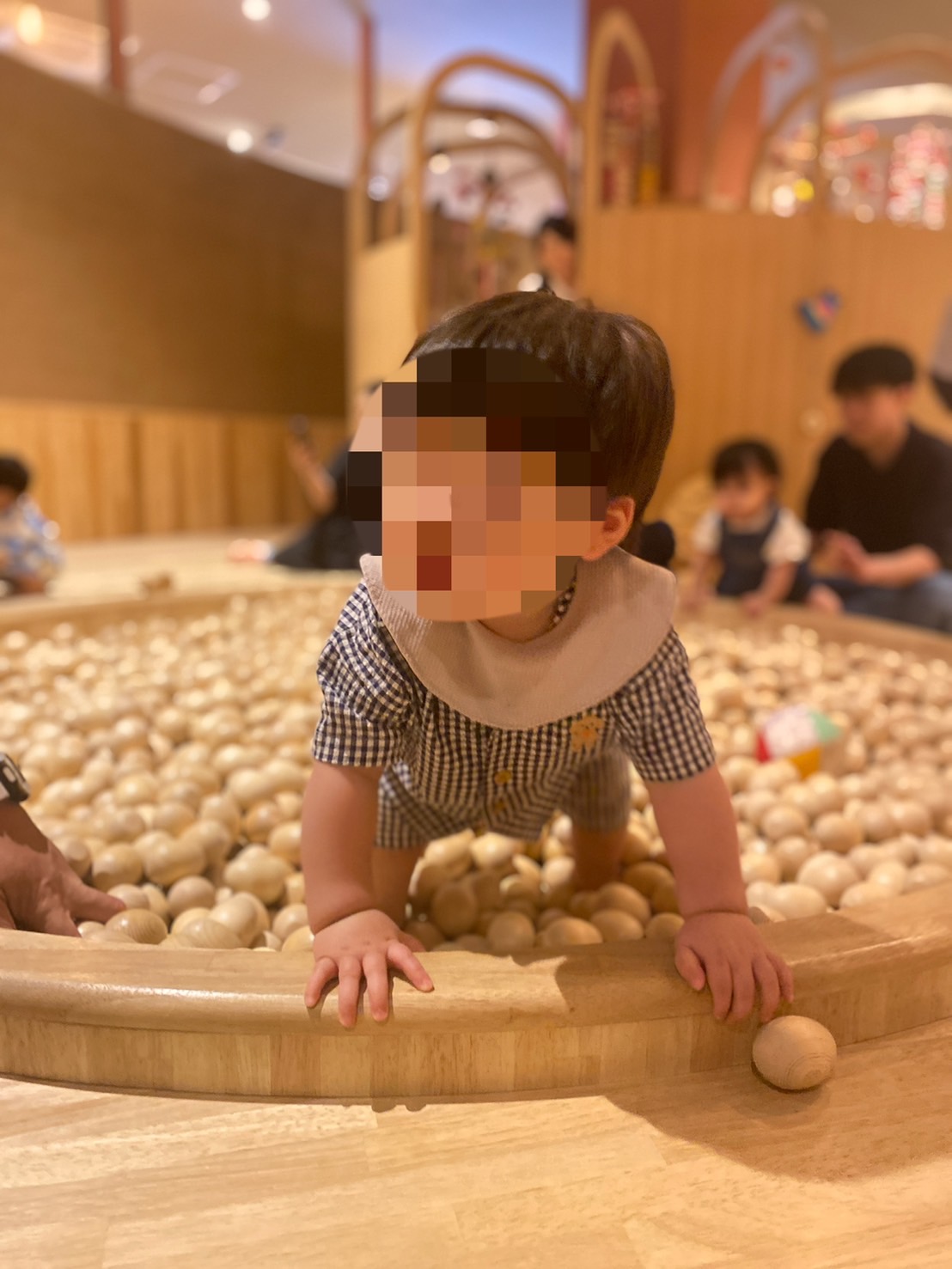 木のボールプールで遊ぶ1歳児。つかまり立ちしながら木製おもちゃに触れている