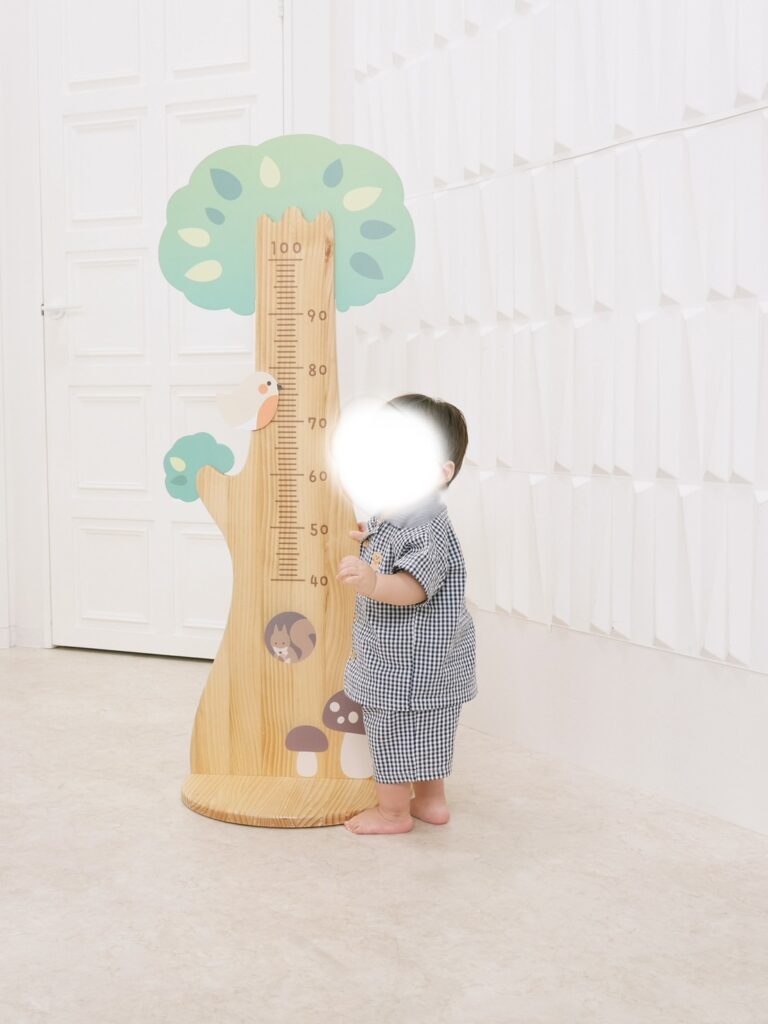 スタジオアリスで身長計の木製ボードの横に立つ1歳児の記念写真