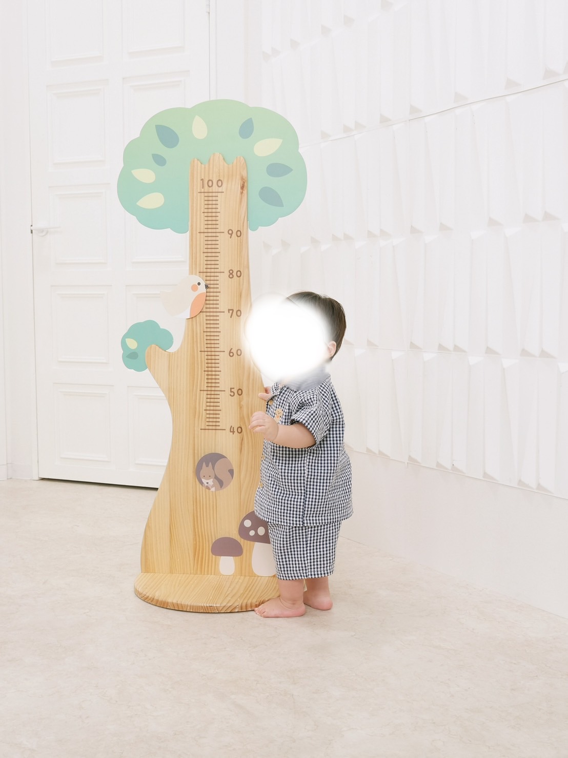 スタジオアリスで身長計の木製ボードの横に立つ1歳児の記念写真